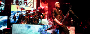 Devin Townsend on stage with drummer and multiple screens behind