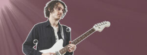 Michael Astley-Brown holding guitar in front of a maroon background
